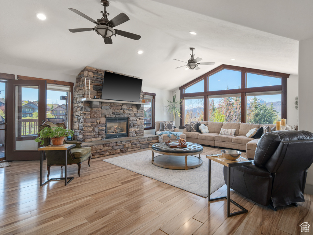 Living area featuring vaulted ceiling, a ceiling fan, a stone fireplace, and wood finished floors