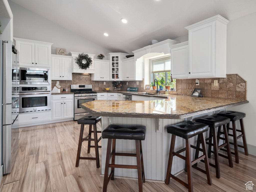 Kitchen featuring appliances with stainless steel finishes, a sink, a peninsula, white cabinetry, and vaulted ceiling