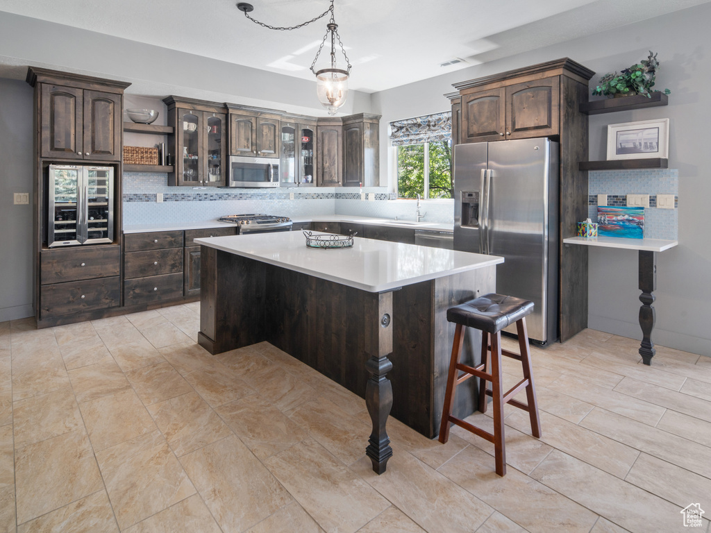 Kitchen featuring backsplash, dark brown cabinets, appliances with stainless steel finishes, and a breakfast bar