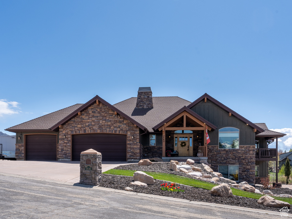 View of front of house with a garage, driveway, roof with shingles, and stone siding