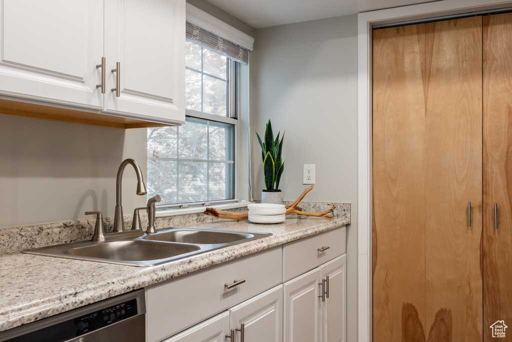 Kitchen featuring stainless steel dishwasher, white cabinetry, a sink, and light countertops