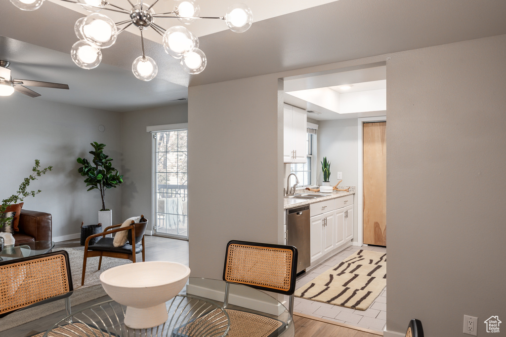 Dining room featuring baseboards, ceiling fan with notable chandelier, light wood-type flooring, and a raised ceiling