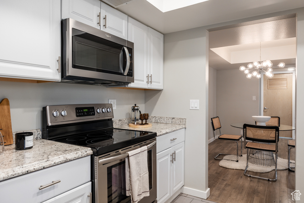 Kitchen with an inviting chandelier, baseboards, white cabinets, light wood-style flooring, and appliances with stainless steel finishes