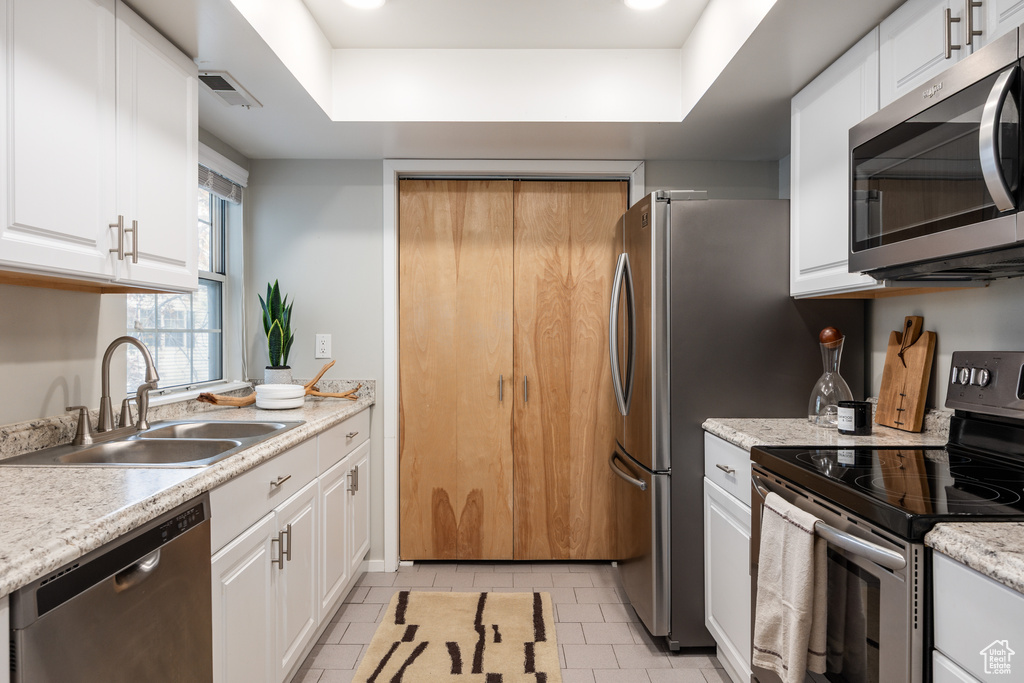 Kitchen with a sink, light tile patterned floors, white cabinets, a raised ceiling, and stainless steel appliances
