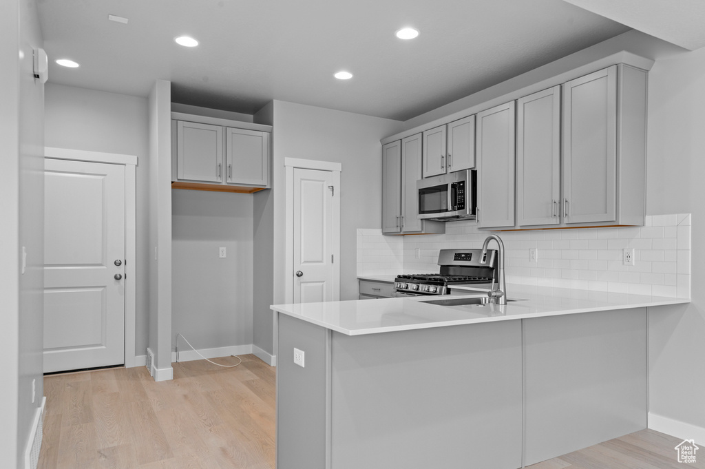 Kitchen with gray cabinets, light wood-type flooring, baseboards, a peninsula, and stainless steel appliances