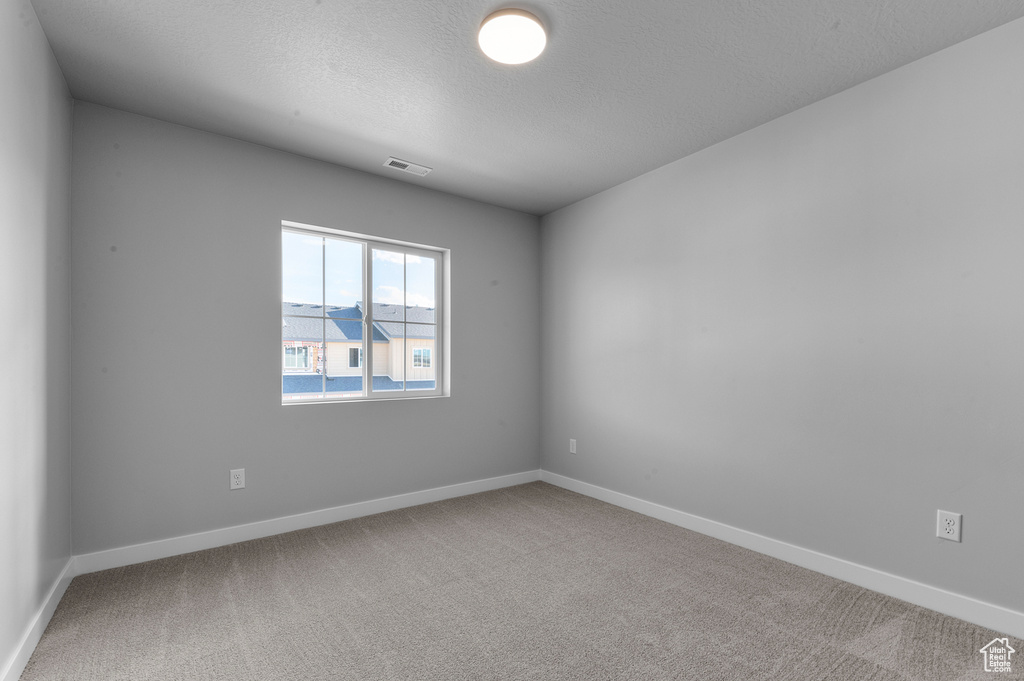 Carpeted empty room with a textured ceiling, baseboards, and visible vents