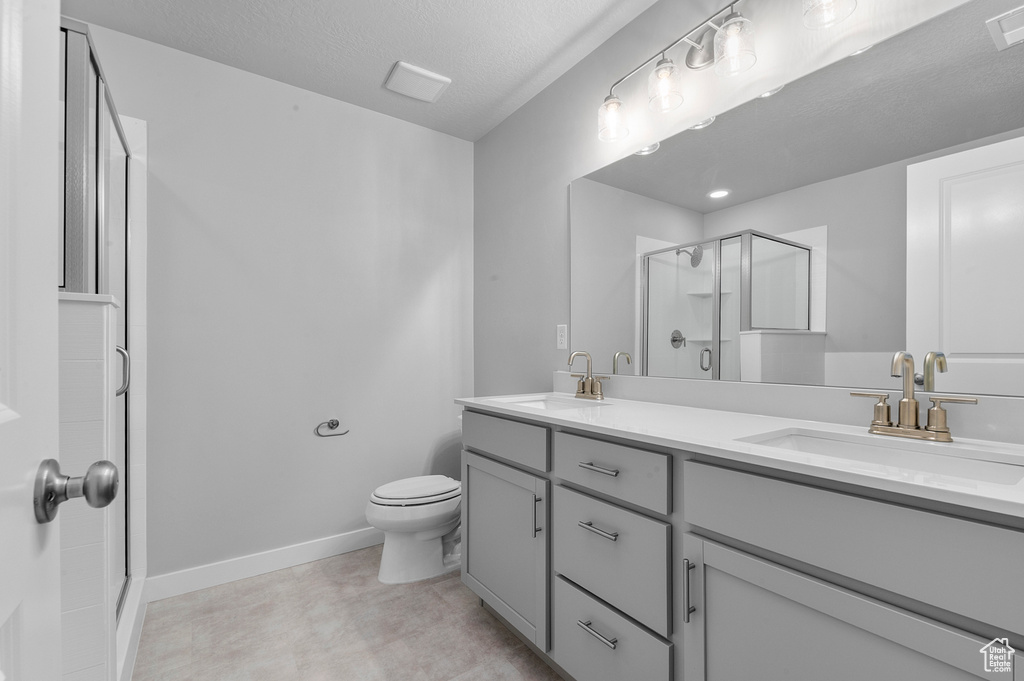 Bathroom with double vanity, a sink, a stall shower, and toilet