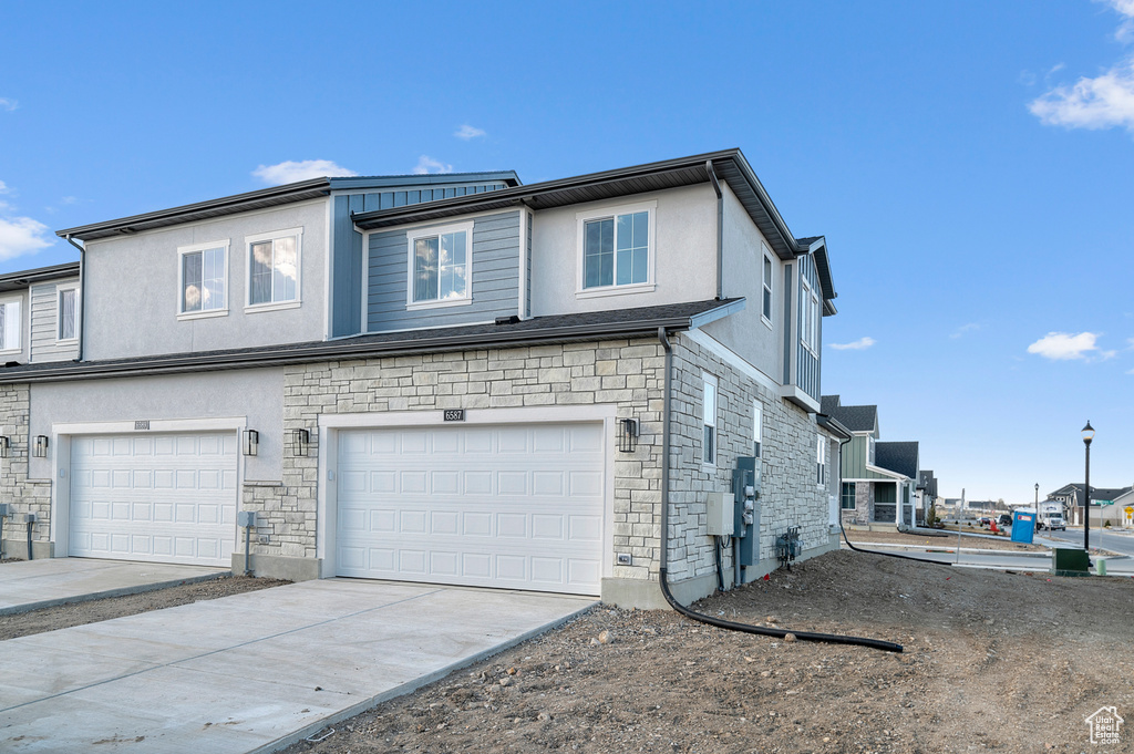 View of home's exterior featuring a garage, stucco siding, driveway, and stone siding