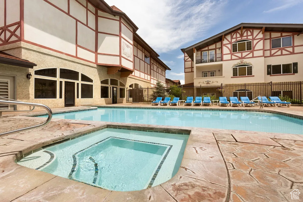 Community pool with a hot tub, a patio, and fence