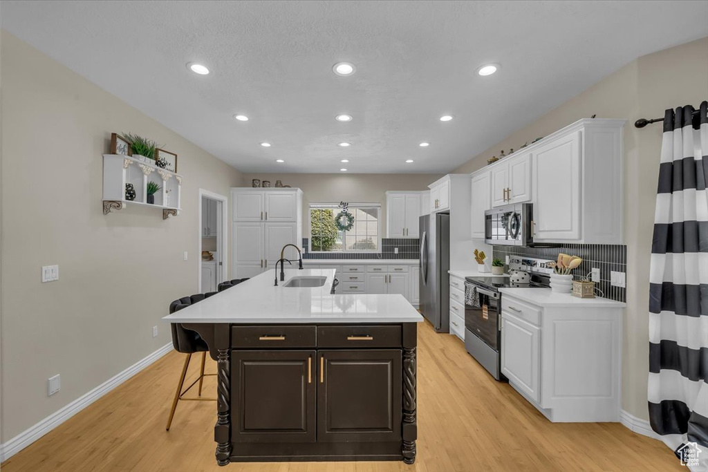 Kitchen featuring white cabinetry, appliances with stainless steel finishes, a sink, and a kitchen bar