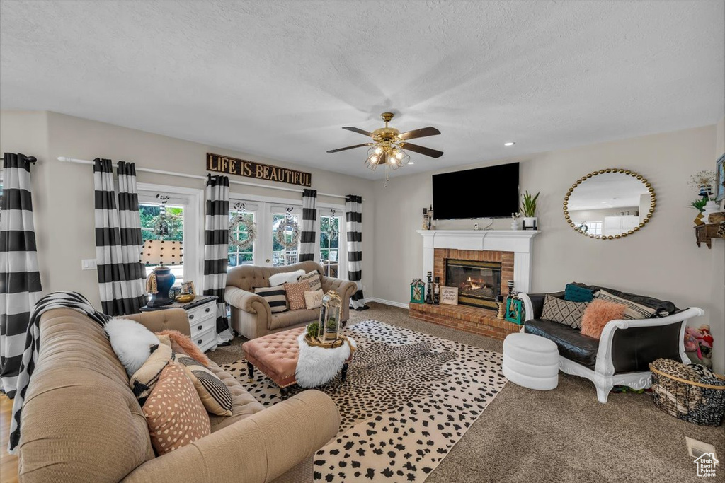 Carpeted living room with baseboards, ceiling fan, a brick fireplace, and a textured ceiling