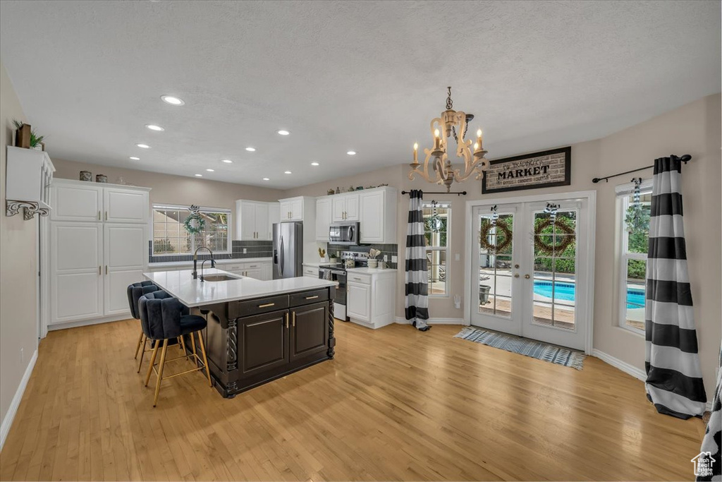 Kitchen with baseboards, light wood-type flooring, a chandelier, a sink, and appliances with stainless steel finishes