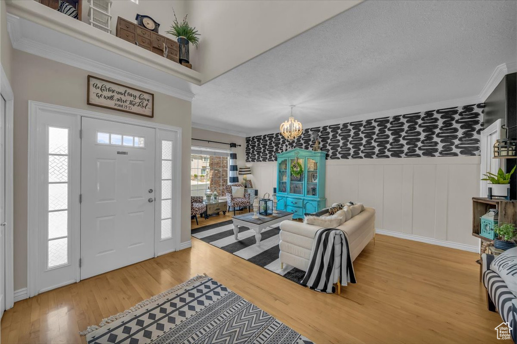 Foyer entrance with crown molding, wainscoting, light wood finished floors, a textured ceiling, and a chandelier