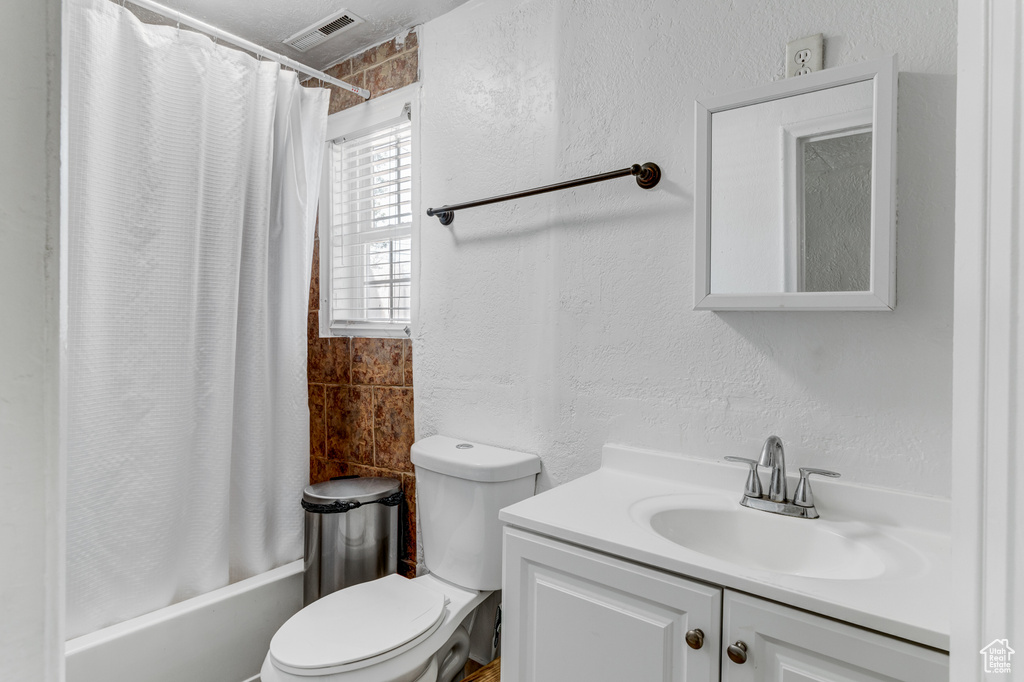 Full bath with vanity, shower / bath combo with shower curtain, a textured wall, visible vents, and toilet
