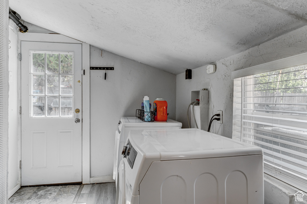 Washroom with independent washer and dryer, a textured ceiling, laundry area, and light wood finished floors