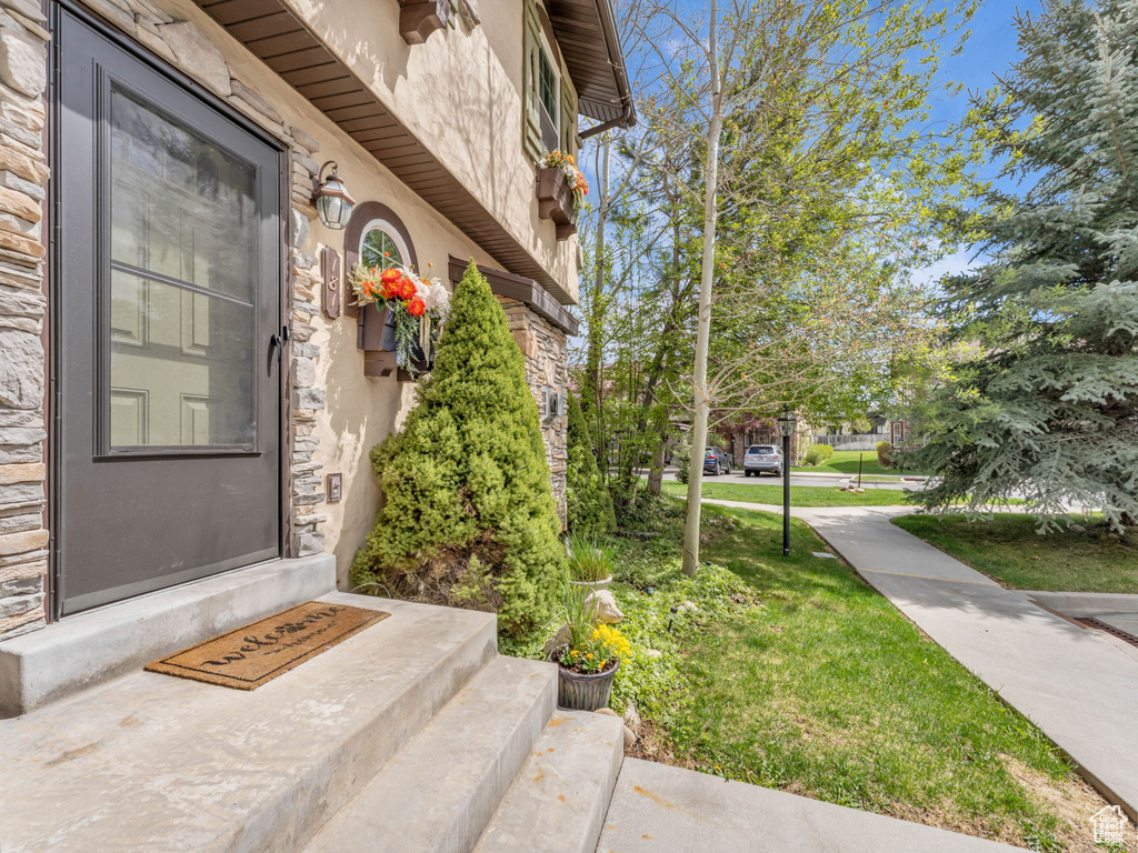 View of exterior entry featuring a lawn, stone siding, and stucco siding
