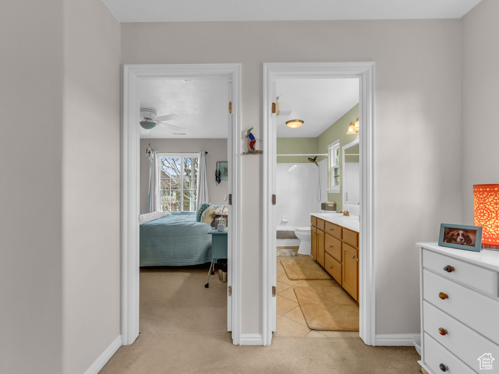 Interior space featuring light colored carpet, connected bathroom, baseboards, and light tile patterned flooring
