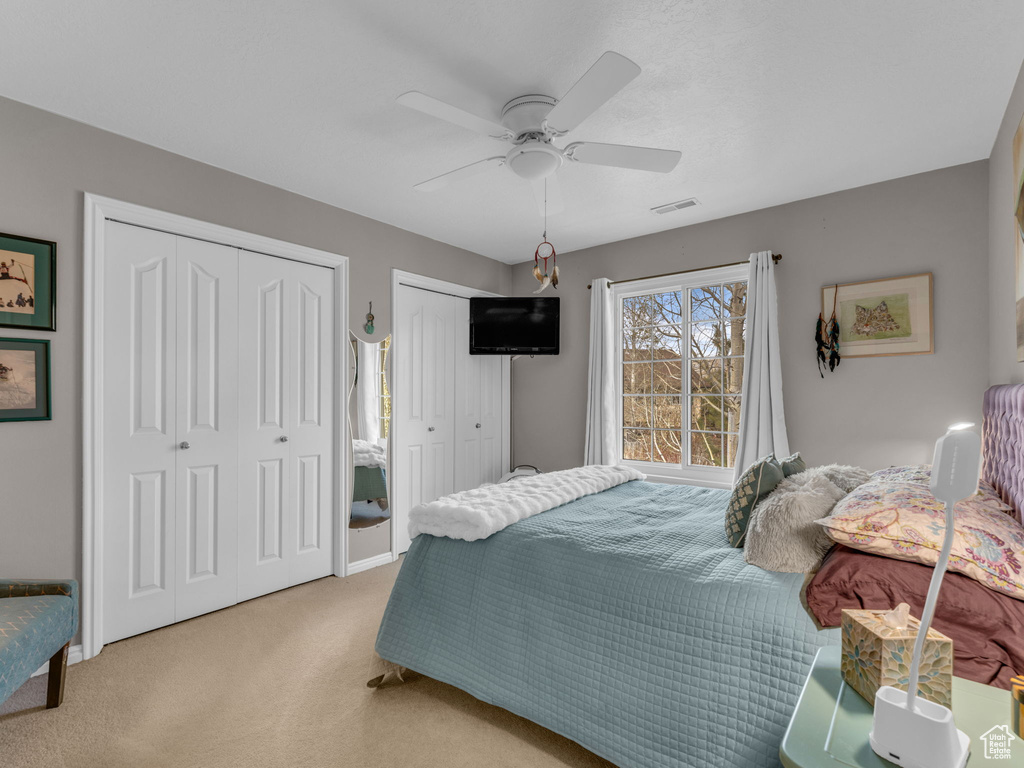 Bedroom featuring two closets, carpet flooring, visible vents, and ceiling fan