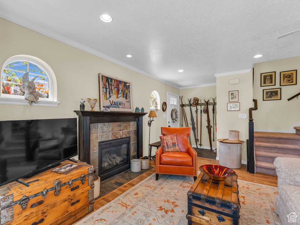 Living room featuring a tiled fireplace, stairs, recessed lighting, wood finished floors, and ornamental molding