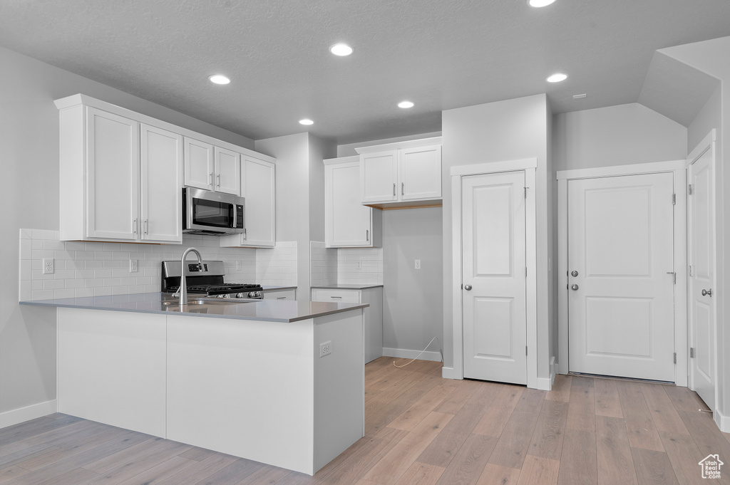 Kitchen featuring a peninsula, baseboards, white cabinets, tasteful backsplash, and appliances with stainless steel finishes