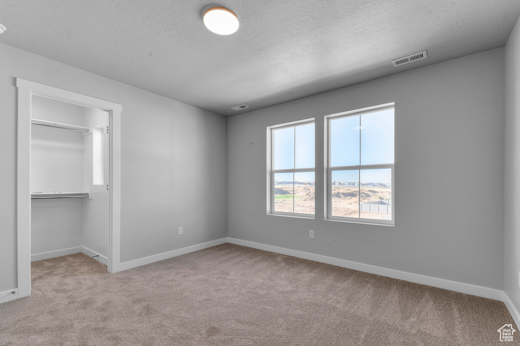 Unfurnished bedroom featuring carpet floors, baseboards, a textured ceiling, and visible vents