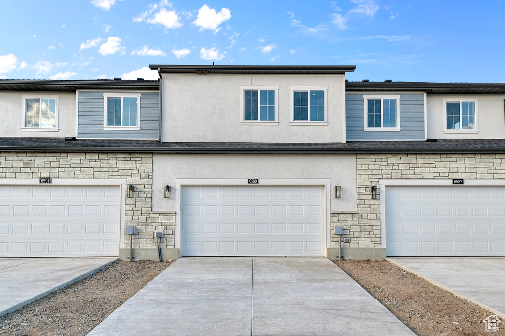 View of property with a garage, stucco siding, and stone siding