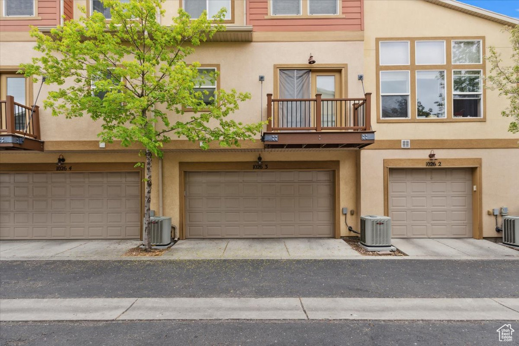View of front facade featuring central air condition unit, an attached garage, and stucco siding