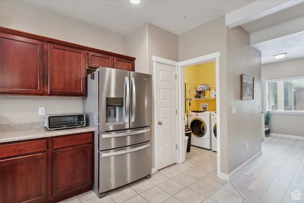 Kitchen with a toaster, washer and dryer, stainless steel refrigerator with ice dispenser, light countertops, and reddish brown cabinets