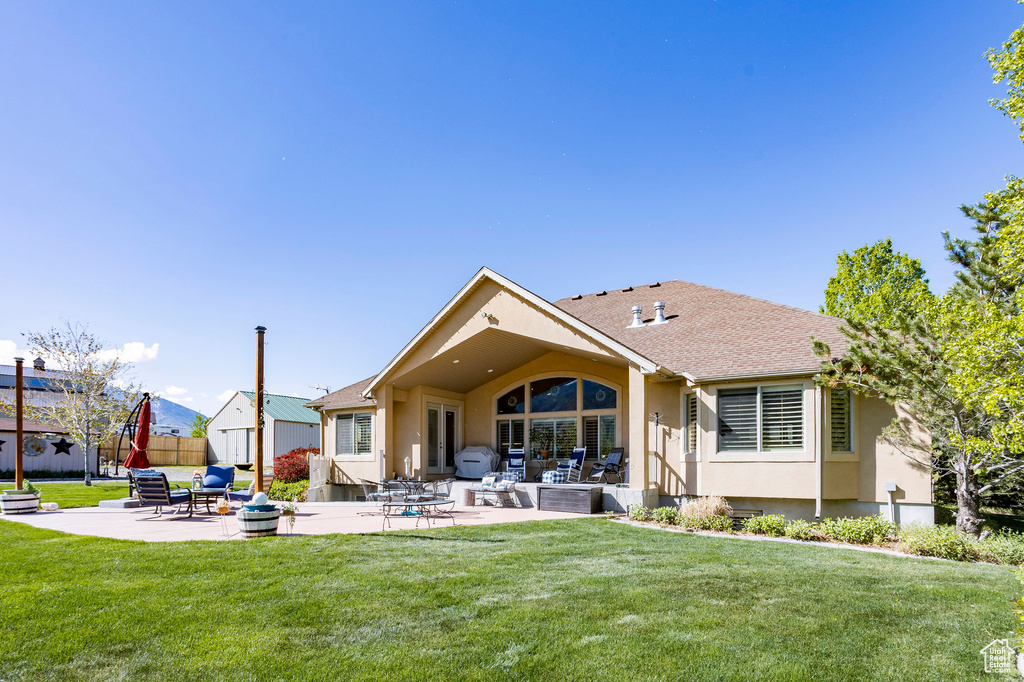 Back of house featuring a lawn, a patio area, stucco siding, and roof with shingles