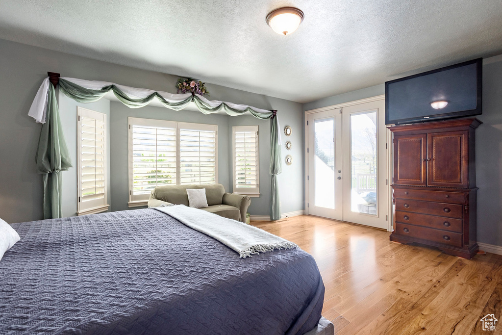 Bedroom featuring french doors, access to outside, multiple windows, light wood-type flooring, and a textured ceiling