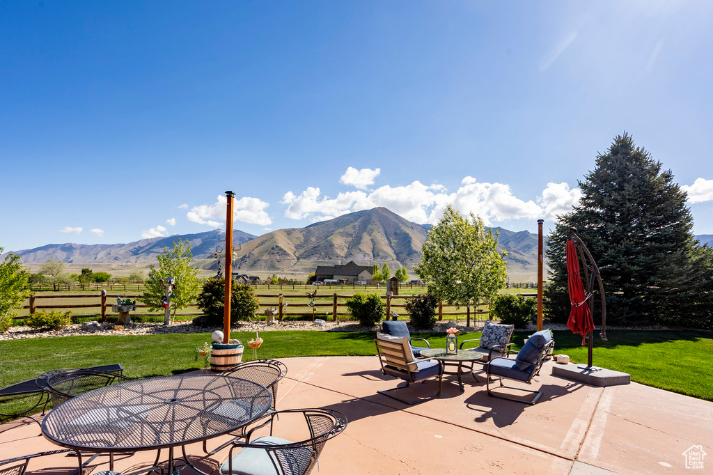 View of patio featuring fence, a mountain view, outdoor dining area, and a rural view