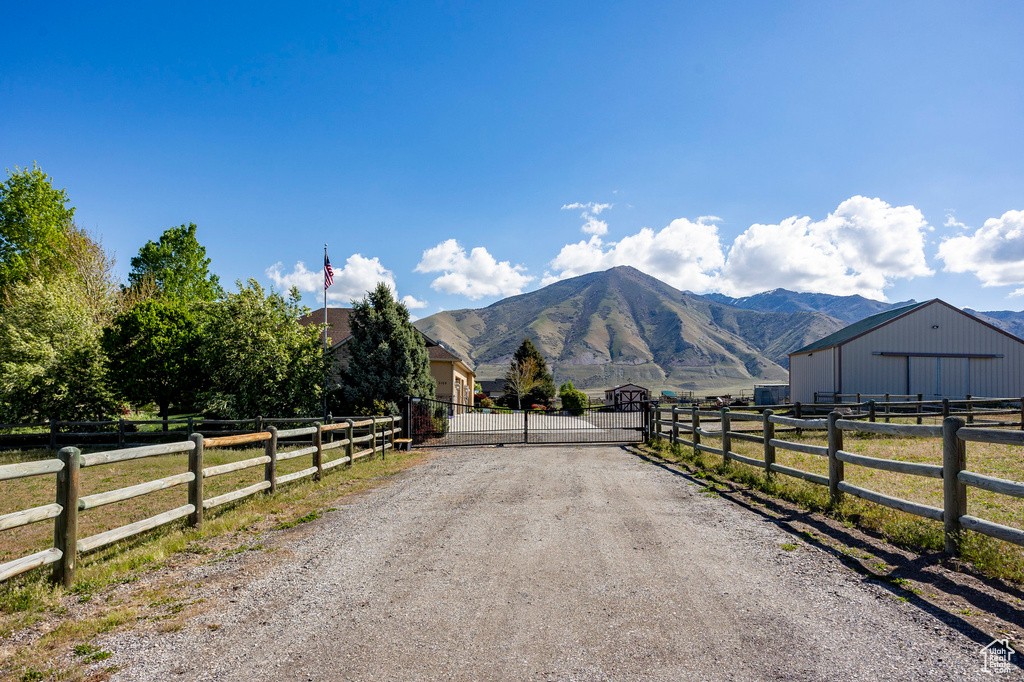 View of road with dirt driveway, a gated entry, a gate, a mountain view, and a rural view