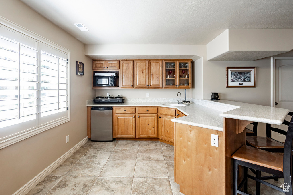 Kitchen with a peninsula, black microwave, glass insert cabinets, a kitchen bar, and a sink