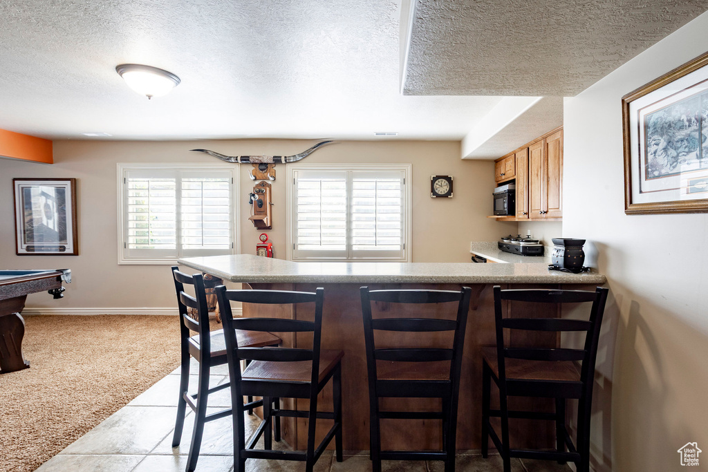 Kitchen featuring a textured ceiling, carpet floors, baseboards, a peninsula, and a breakfast bar