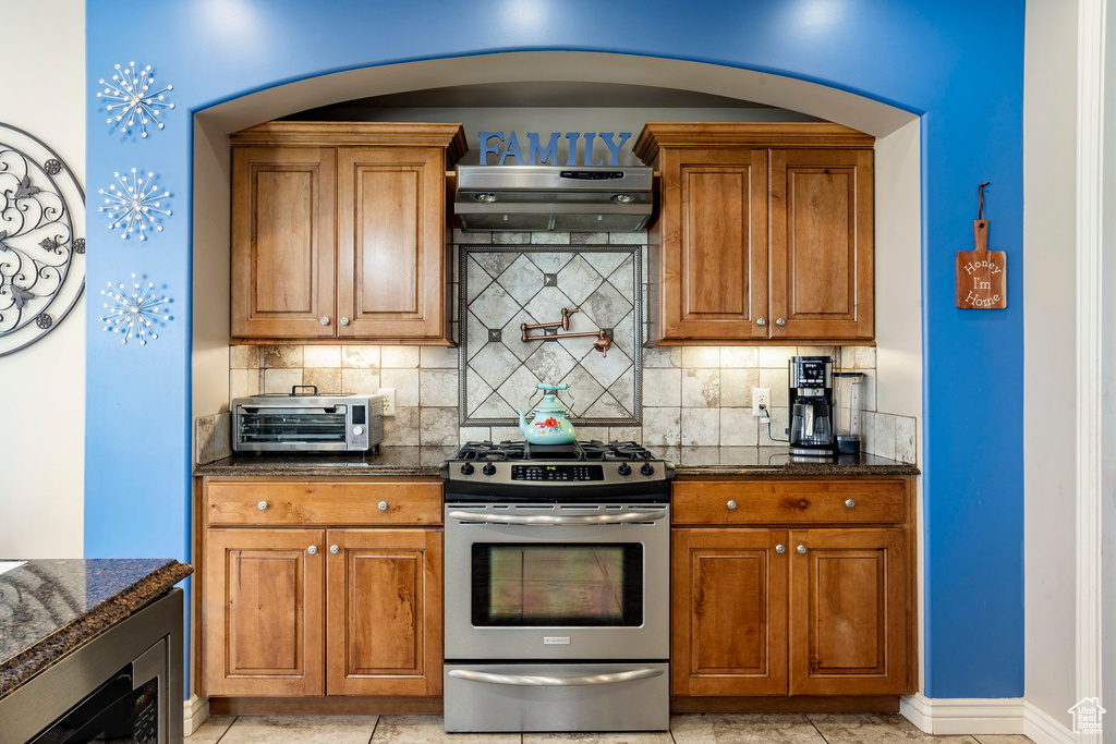 Kitchen with a toaster, stainless steel range with gas stovetop, brown cabinetry, and under cabinet range hood
