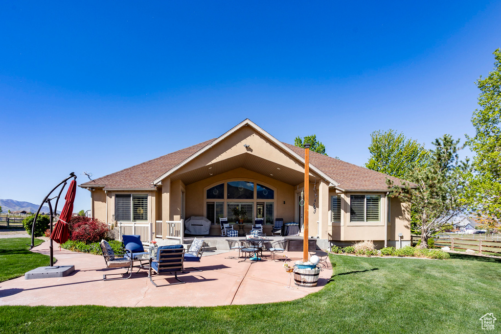 Rear view of property with a lawn, a patio area, fence, a shingled roof, and stucco siding