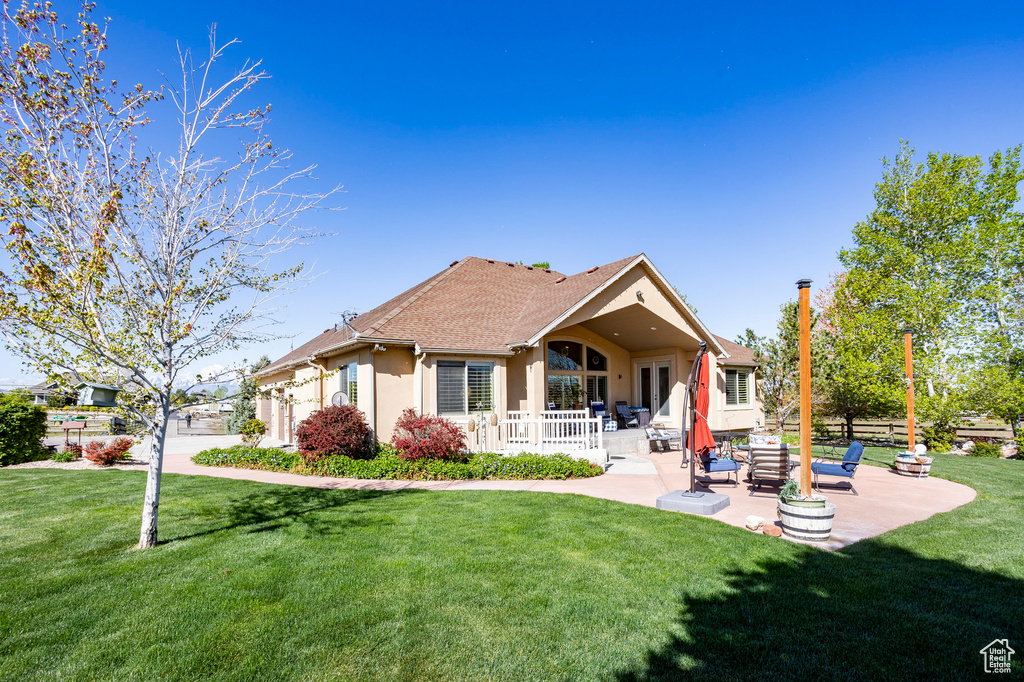 Rear view of property with a shingled roof, stucco siding, a yard, and a patio area