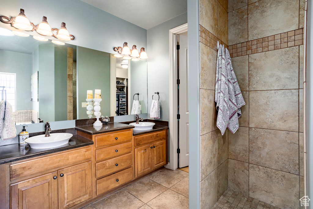 Full bath with double vanity, tile patterned floors, tiled shower, and a sink