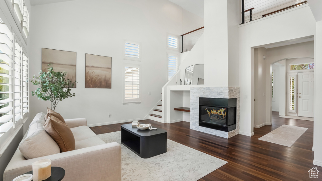 Living room featuring arched walkways, dark wood-style flooring, stairs, and a towering ceiling