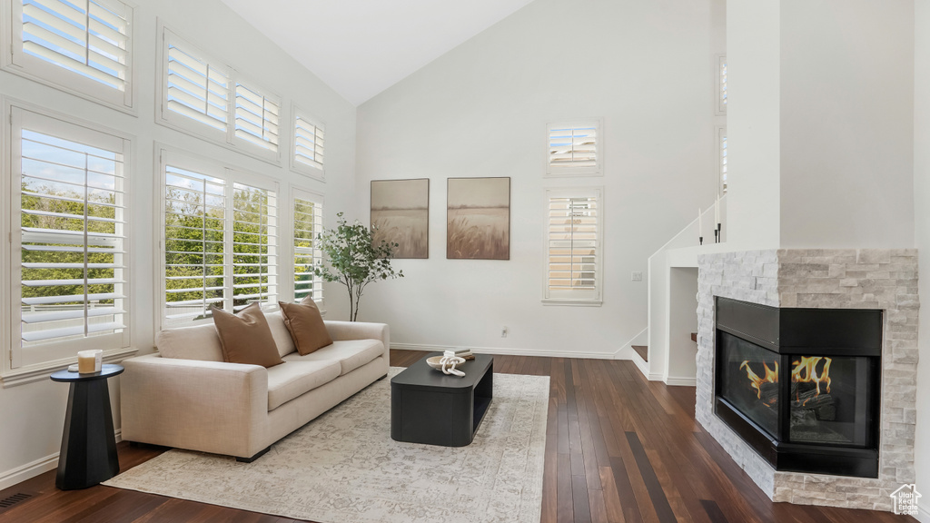 Living area featuring a fireplace, high vaulted ceiling, baseboards, and dark wood-type flooring
