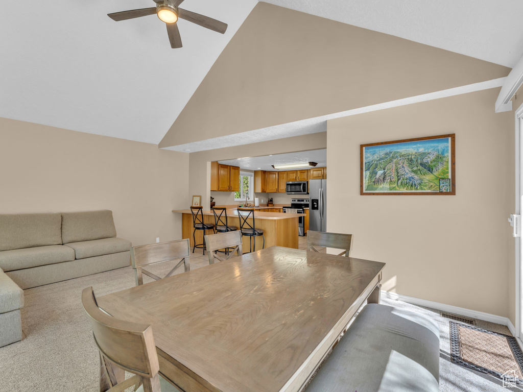 Dining room featuring high vaulted ceiling, visible vents, light carpet, and ceiling fan