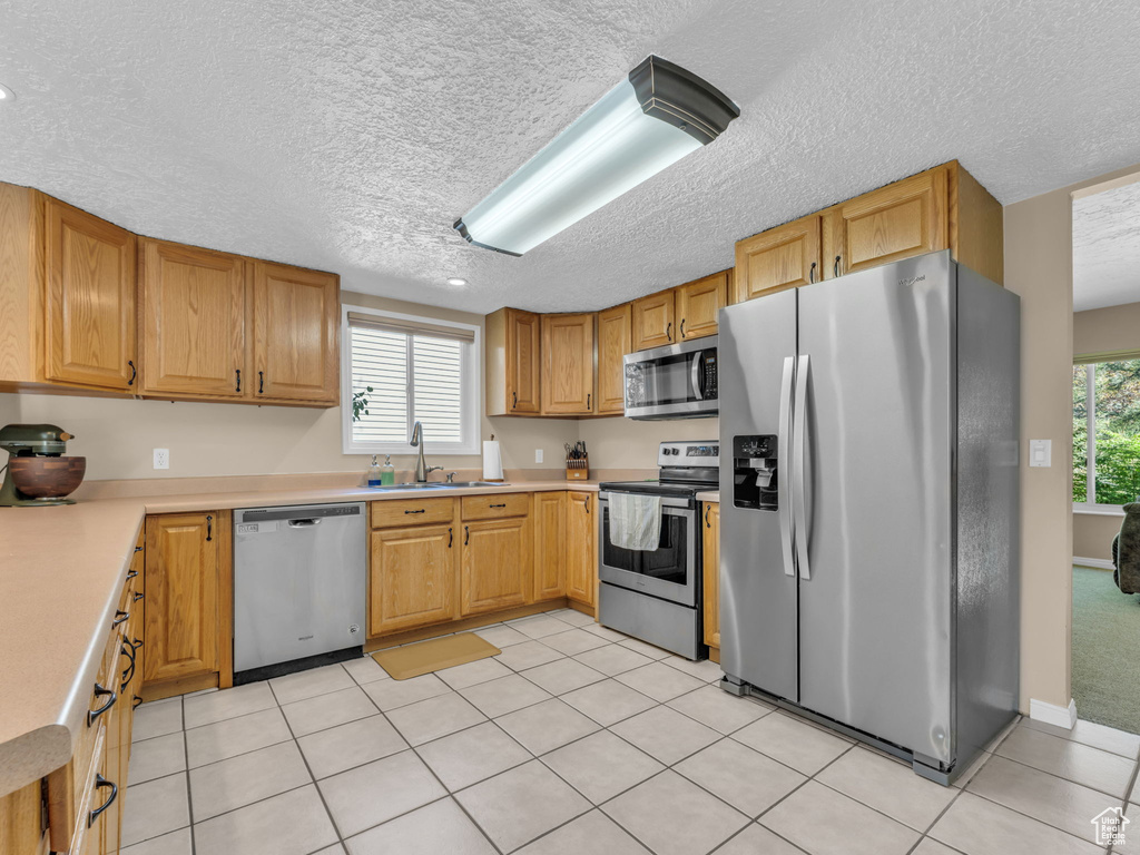 Kitchen featuring a sink, a textured ceiling, appliances with stainless steel finishes, and light countertops