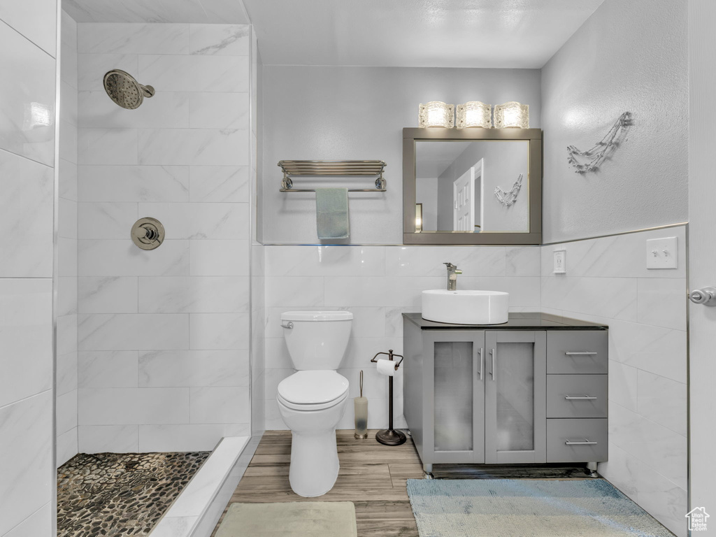 Bathroom featuring vanity, wood finished floors, toilet, tile walls, and a tile shower