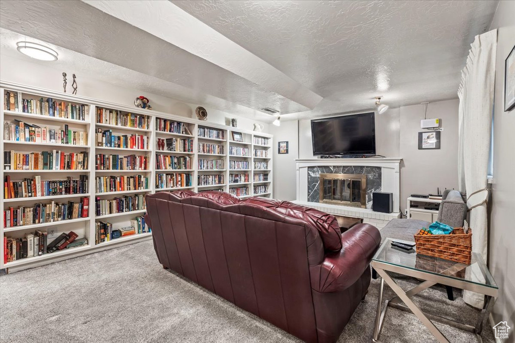 Carpeted living room featuring wall of books, a textured ceiling, and a premium fireplace
