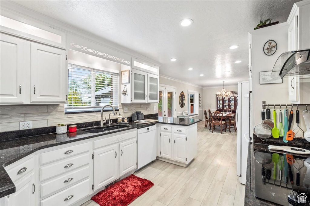 Kitchen with crown molding, a peninsula, white appliances, white cabinets, and a sink