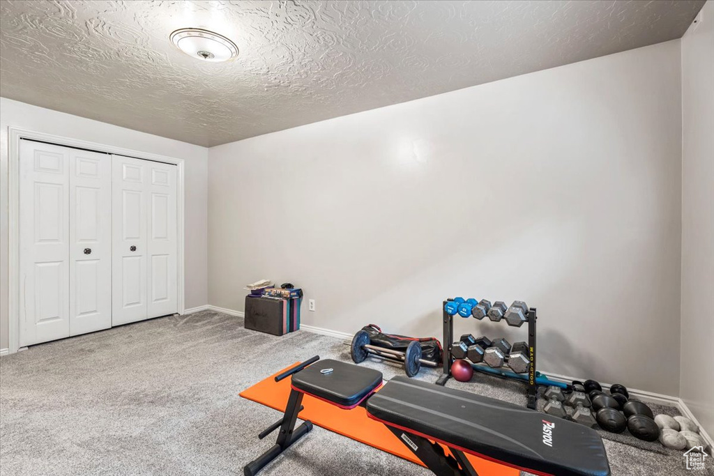 Exercise area featuring baseboards, carpet, and a textured ceiling