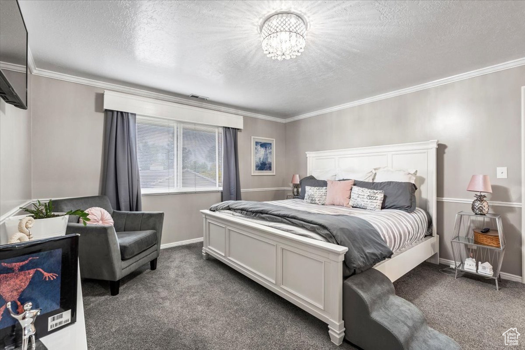 Carpeted bedroom with a textured ceiling, visible vents, baseboards, a notable chandelier, and ornamental molding