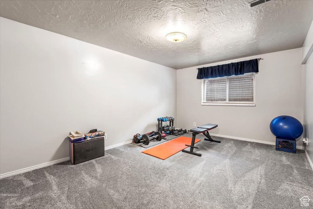 Workout area with carpet floors, a textured ceiling, and baseboards