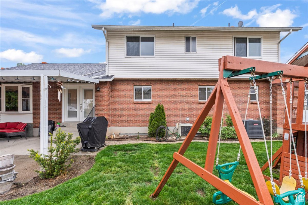 Rear view of house featuring cooling unit, brick siding, a playground, a patio area, and a yard