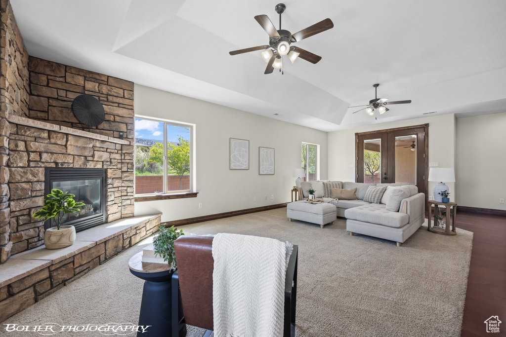 Carpeted living room featuring ceiling fan, a raised ceiling, a fireplace, baseboards, and lofted ceiling